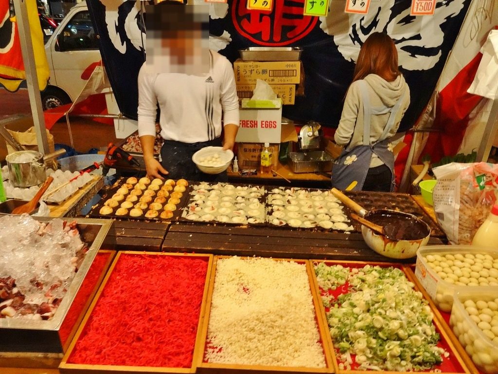 A takoyaki stall with trays of pickled ginger, tempura bits and green onion